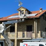 installazione di impianto solare termico su una casa in pietra, con operai al lavoro su una piattaforma elevatrice. Mezzi della ditta Cavelli Giorgio & C in primo piano.