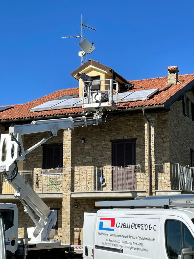 Installazione di impianto solare termico su una casa in pietra, con operai al lavoro su una piattaforma elevatrice. Mezzi della ditta Cavelli Giorgio & C in primo piano.